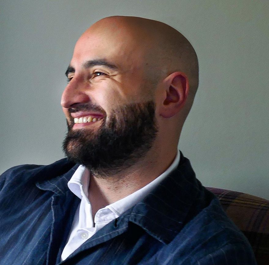 Davuud Ghani, smiling, in a dark jacket and open-collared shirt